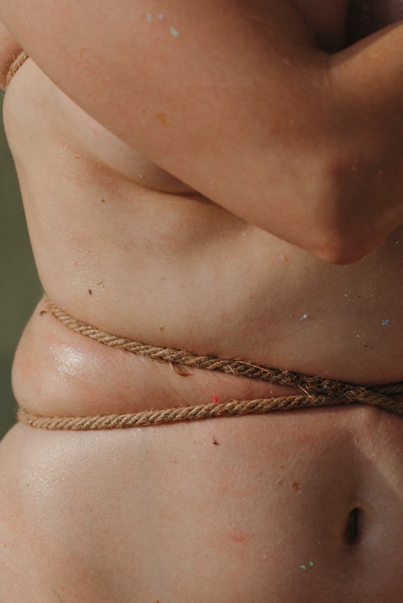 Crop shot of unrecognizable female's body corded with rope. Conceptual shot about self rejection, imperfection and pain