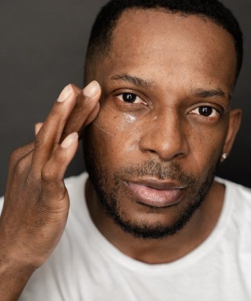 Close up of black man using eye cream. Studio  shot.